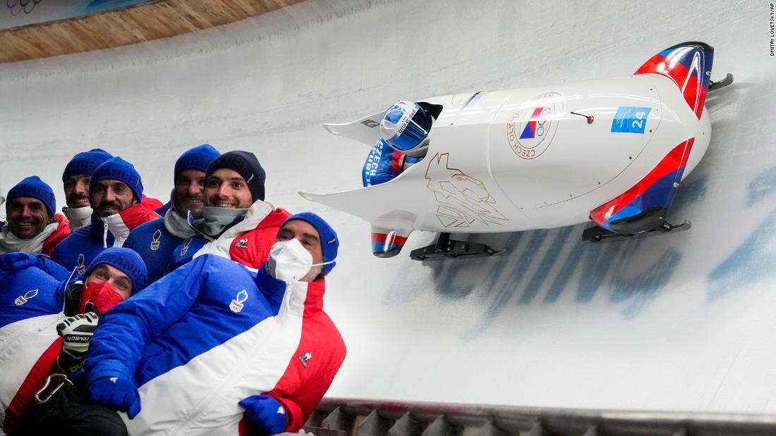 Members of the Czech Republic team pose for a photo as teammates Dominik Dvorak and Jakub Nosek slide past in a bobsled on Monday, February 14.