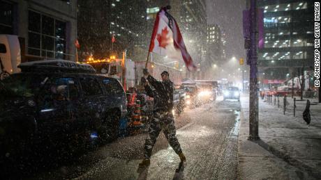 Snow falls around a demonstrator waving a flag  outside  parliament in Ottawa on February 17, 2022.