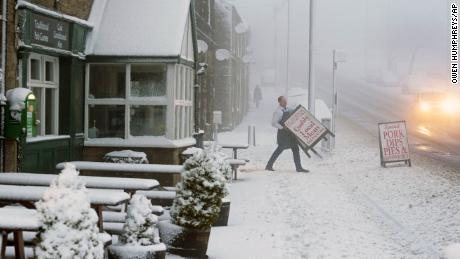 A local butcher carries his shop sign across a snowy pavement in County Durham, Britain, as Storm Eunice makes landfall.
