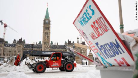 Machinery moves a concrete barricade past the Parliament buildings while a protest sign sits in a garbage container in Ottawa on Sunday, February 20.