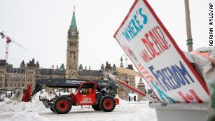Machinery moves a concrete barricade past the Parliament buildings while a protest sign sits in a garbage container in Ottawa on Sunday, February 20.
