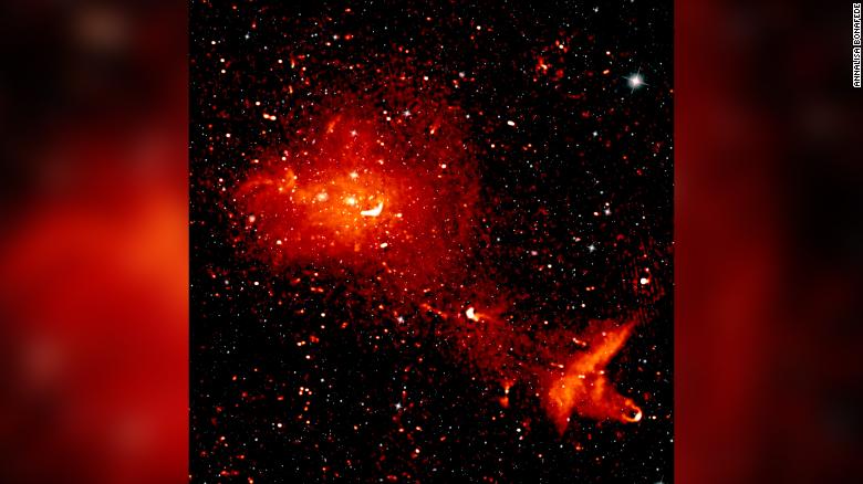 A composite radio (red) and infrared (white) image depicts the Coma cluster, which is over 300 million light-years from Earth and consists of over 1,000 individual galaxies. The radio image shows radiation from highly energetic particles that pervade the space between the galaxies. 
