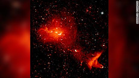 A composite radio (red) and infrared (white) image depicts the Coma cluster, which is over 300 million light-years from Earth and consists of over 1,000 individual galaxies. The radio image shows radiation from highly energetic particles that pervade the space between the galaxies. 