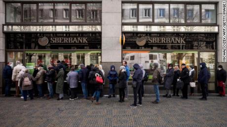 People queue outside a branch of Russian state-owned bank Sberbank to withdraw their savings and close their accounts in Prague on February 25, 2022, before Sberbank will close all its branches in the Czech Republic later in the day. - US President Biden was the first to announce sanctions, hours after Russian President Putin declared a &quot;military operation&quot; into Ukraine. The first tranche will hit four Russian banks -- including the country&#39;s two largest, Sberbank and VTB Bank -- cut off more than half of Russia&#39;s technology imports, and target several of the country&#39;s oligarchs. (Photo by Michal Cizek / AFP) (Photo by MICHAL CIZEK/AFP via Getty Images)