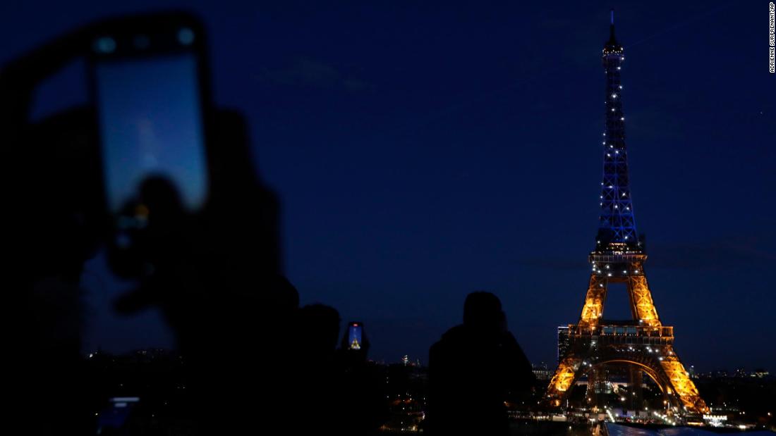 People photograph Paris&#39; Eiffel Tower as it is lit with Ukraine&#39;s colors on February 25.
