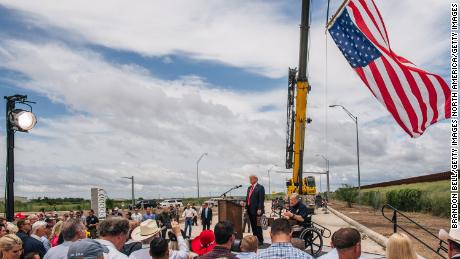 People listen to Texas Gov. Greg Abbott&#39;s address, during a tour to an unfinished section of the border wall with former President Donald Trump on June 30, 2021 in Pharr, Texas. 