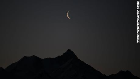 A picture taken early on February 27, 2022 shows a crescent of moon above the 4506 meters high Weisshorn mountain in the Swiss alps from Crans-Montana, Switzerland. 