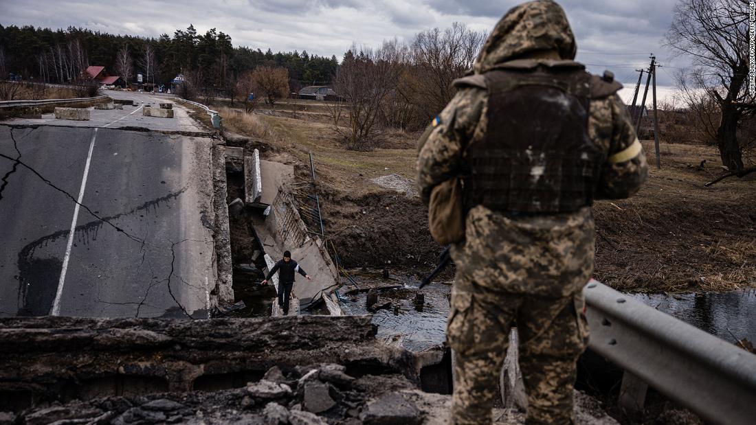 A Ukrainian serviceman watches a civilian cross a blown-up bridge in a Ukrainian village east of the town of Brovary on March 6.