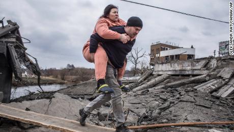 Un hombre carga a una mujer mientras cruza una ruta mejorada mientras huye de Irbine en Ucrania el domingo.