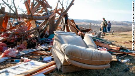 People stand among debris Monday as cleanup efforts are underway in Winterset, Iowa, after a tornado tore through the area Saturday. 