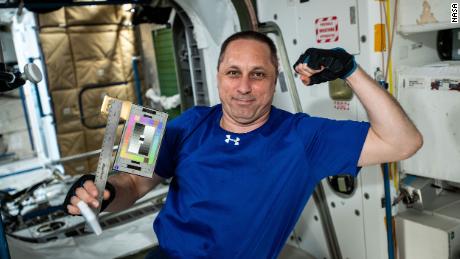 Российский космонавт Антон Шкаплеров позирует с линейкой и цветной картой для проведения эксперимента в области космической археологии.
