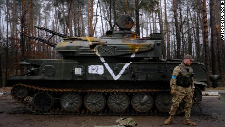 Un miembro de las Fuerzas de Defensa Regionales de Ucrania inspecciona un vehículo blindado ruso destruido en la autopista E-40.