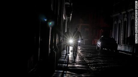 A vehicle&#39;s headlights illuminate people walking on a dark street in San Juan, Puerto Rico, after a power outage on the island Wednesday. 