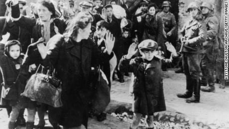 This 1943 photograph, from an official SS report, shows Jewish civilians held at gunpoint by Nazi SS troops after being forced out of a bunker where they were sheltering during the Warsaw Ghetto Uprising.