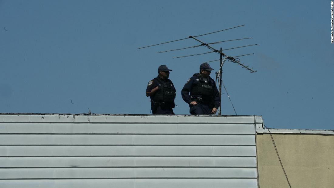 New York City police officers look down from a rooftop.