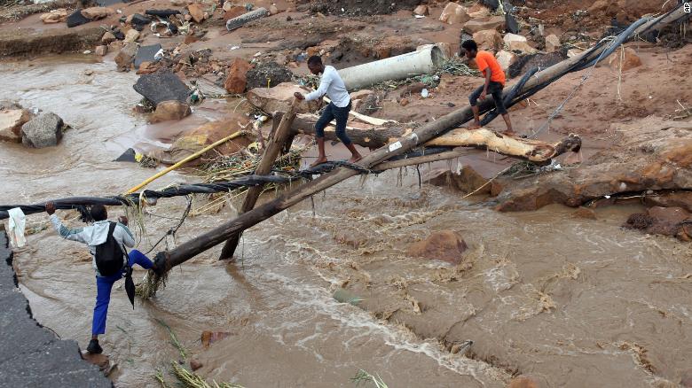 People walk across a makeshift bridge over a river, after a bridge was swept away in Ntuzuma, outside Durban, South Africa, Tuesday, April 12, 2022.