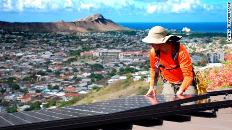 Dane Hew Len, lead installer for RevoluSun, places a solar panel on a roof in Honolulu.