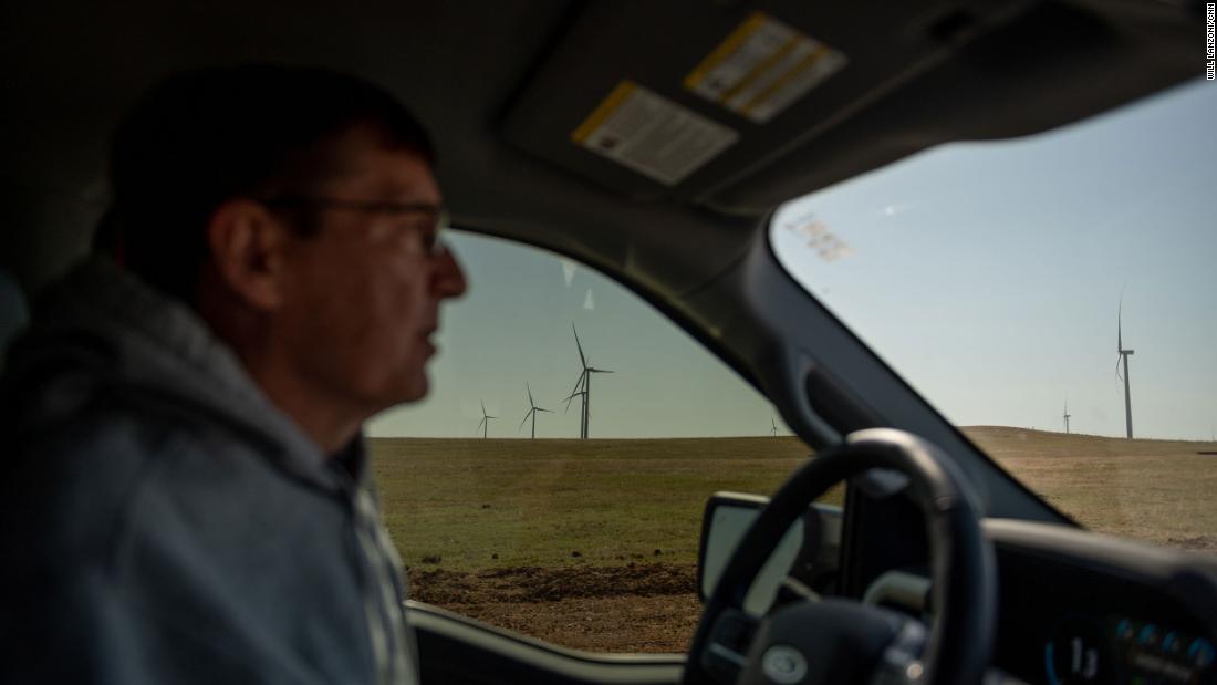 Wind turbines are seen in the distance from Scott Hampton&#39;s truck as he drives on a county road in Weatherford.