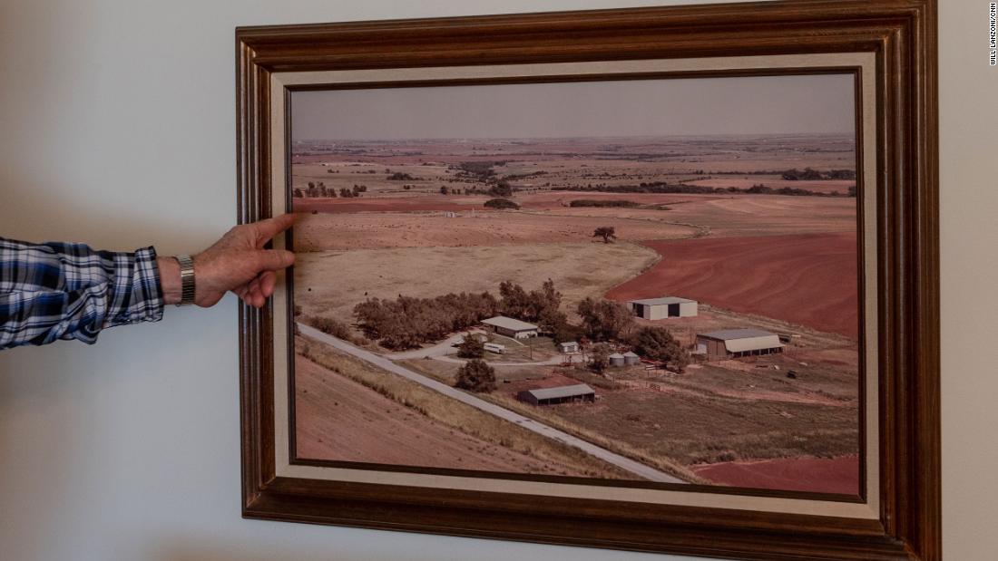 Terry Baker points to a photograph hanging on the wall of Cathy Baker&#39;s childhood home showing the family farm in the late 1900s.