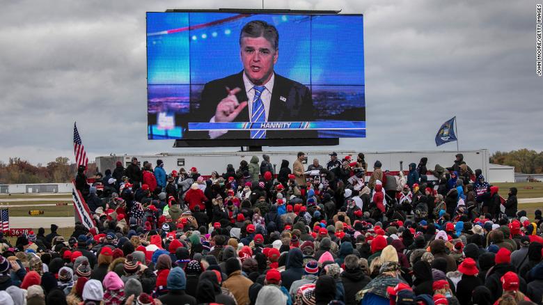 Supporters of U.S. President Donald Trump watch a video featuring Fox host Sean Hannity ahead of Trump&#39;s arrival to a campaign rally in Michigan on October 30, 2020.
