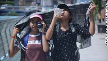 In the scorching heat of the afternoon in Mumbai, India, two young girls walk and cover their heads while drinking water.