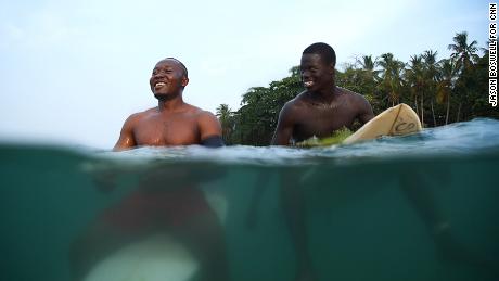 Philip Banini and Massalley Comney share a joke in the waters off the coast of Robertsport, Liberia. The seaside community has become popular among surfers, transforming it into an international tourist destination. 