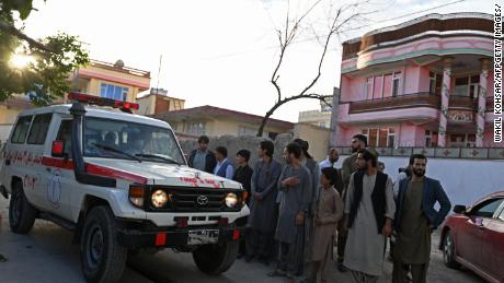Onlookers stand next to an ambulance carrying victims near the site of a blast in Kabul on April 29, 2022. 