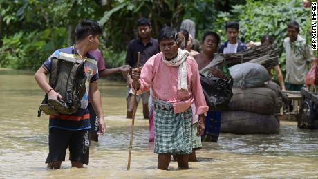 Ľudia kráčajú v záplavových vodách v okrese Nagoon v indickom štáte Assam 18. mája.