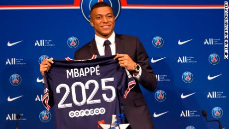 Mbappé poses holding a shirt during a press conference.