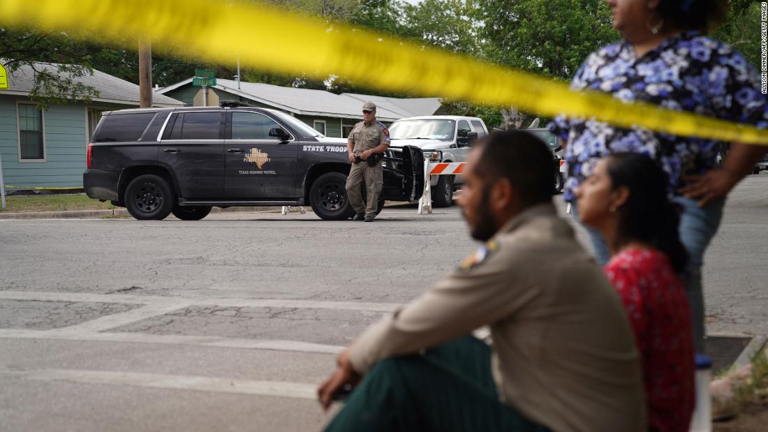 People sit on the curb outside of the school as state troopers guard the area Tuesday.