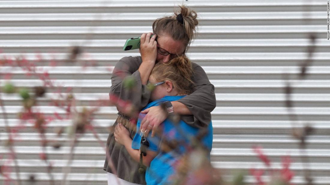 A woman cries and hugs a young girl while on the phone outside the civic center in Uvalde.