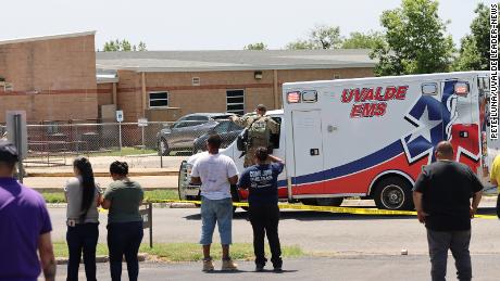 An ambulance waits at Robb Elementary School as people watch from behind police tape in Uvalde, Texas, on May 24, 2022.