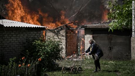An elderly woman walks away from the garage of a burning house after shelling the town of Lysytsansk in eastern Ukraine's Donbass region on May 30, 2022.