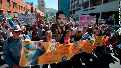 Thousands of people march through the city centre, to the South African Parliament, waving South African flags and banners, to call for the South African president to step down on April 7, 2017, in Cape Town. The protest comes after South African President Jacob Zuma dismissed widely respected South African Minister of finance, Pravin Gordhan in a cabinet reshuffle. The move by Zuma has caused the South African economy to be given a &#39;junk&#39; rating by two of the international financial ratings agencies widely seen as a move to allow a controversial nuclear deal with Russia to go through, as well as allowing the Gupta family to buy a bank in the country, neither of which Gordhan would allow as Minister of Finance. A cut-out poster of Atul Gupta is visible. / AFP PHOTO / RODGER BOSCH        (Photo credit should read RODGER BOSCH/AFP via Getty Images)