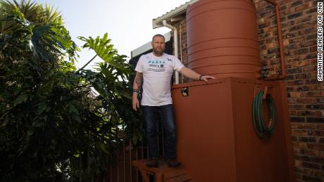 Rhett Saayman de pie junto a uno de sus varios tanques de agua en su casa en Kamma Heights.