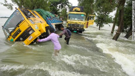 People wade past stranded trucks on a flooded street in Sunamganj, Bangladesh on June 21, 2022.