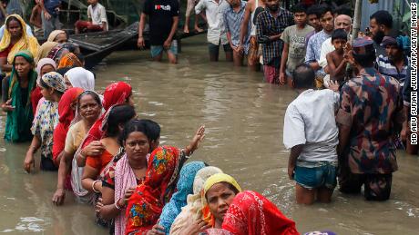Door de overstroming getroffen mensen staan ​​in de kniediepe overstromingswateren om voedselhulp te verzamelen na zware moessonregens in het district Sunamganj, Bangladesh op 21 juni 2022.