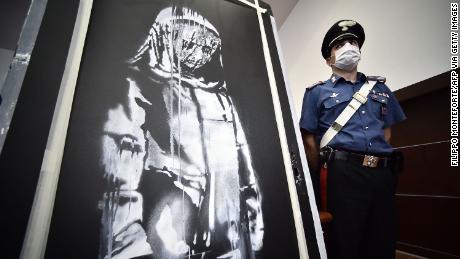 A policeman stands guard near a piece of art attributed to Banksy, that was stolen at the Bataclan in Paris in 2019, and found in Italy, ahead of a press conference in L&#39;Aquila on June 11, 2020. - The work was found in an abandoned farmhouse in Abruzzo, l&#39;Aquila prosecutor informed on June 10, 2020. (Photo by Filippo MONTEFORTE / AFP) / RESTRICTED TO EDITORIAL USE - MANDATORY MENTION OF THE ARTIST UPON PUBLICATION - TO ILLUSTRATE THE EVENT AS SPECIFIED IN THE CAPTION (Photo by FILIPPO MONTEFORTE/AFP via Getty Images)