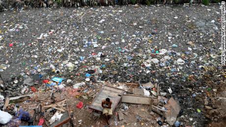 A man sits on a cart next to a sewer canal filled with plastics and other waste in New Delhi on June 30, 2022. 