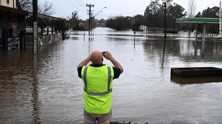 A local takes a photo of a road inundated by floodwaters in Camden in South Western Sydney, Sunday, July 3, 2022.