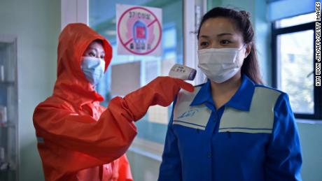 Seorang pekerja kesehatan di Pabrik Kosmetik Pyongyang mengukur suhu tubuh seorang wanita yang tiba untuk shiftnya pada 16 Juni.
