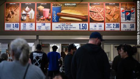 Customers line up to order the $1.50 Costco Kirkland Signature hot dog and soda combo under signage.