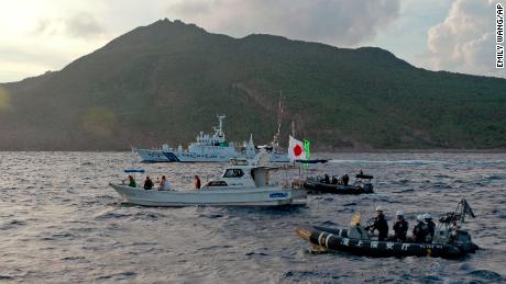 2013年8月、日本の沿岸警備隊の船は、中国のディオユと日本の尖閣として知られる紛争中の島々の近くで、旗を掲げた日本の活動家の漁船で航行します。 