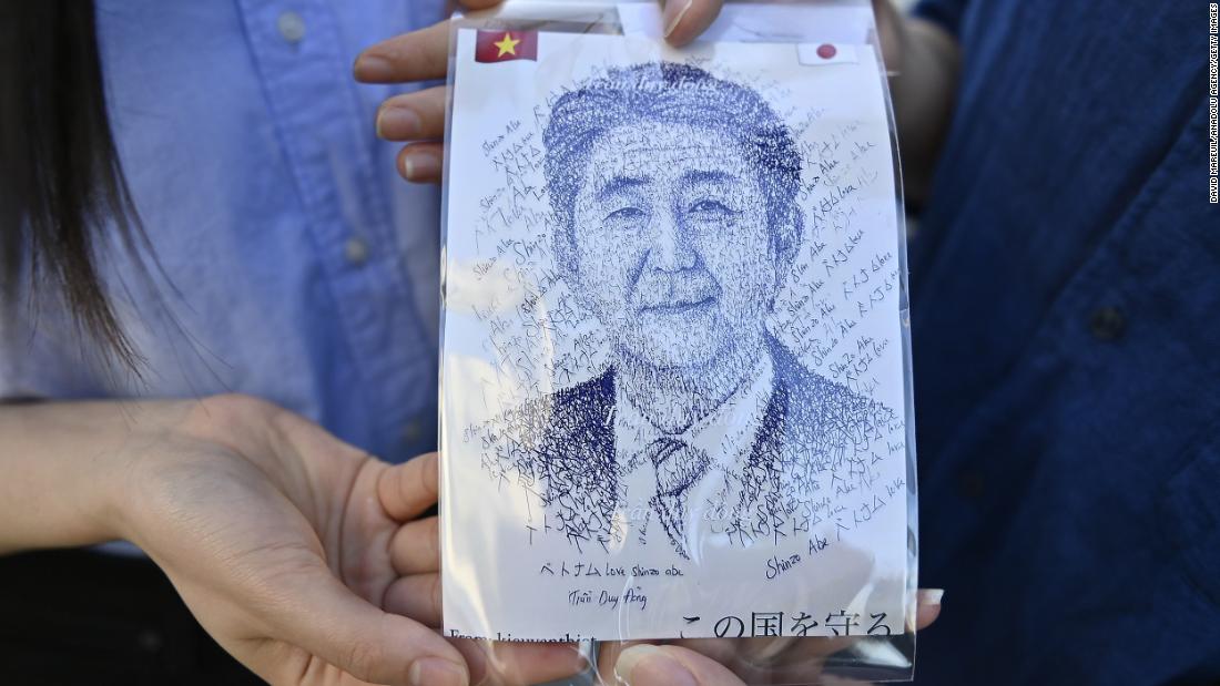 A couple show an illustration of Shinzo Abe as they pay homage in front of his residence in Tokyo, Japan, on July 10.