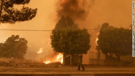 Um membro das forças armadas caminha perto de um incêndio florestal em Palmela, Portugal, em 13 de julho.  O fogo está atualmente perto de um posto de gasolina.  Em um esforço para salvar suas vidas, algumas pessoas e animais são evacuados. 