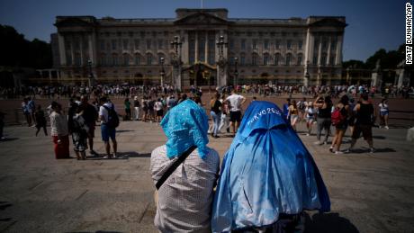 People shield their heads from the sun on Monday after a scaled down version of the Changing of the Guard ceremony took place outside Buckingham Palace in London during an extreme heat wave.