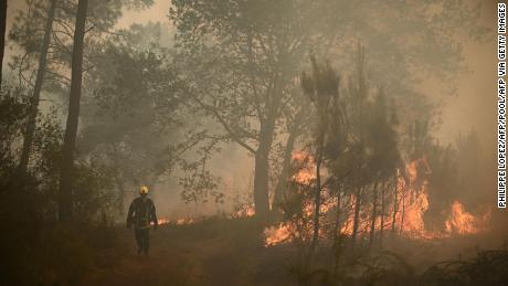 A firefighter walks among flames at a forest fire near Louchats, some 35kms from Landiras in Gironde, southwestern France on July 18, 2022. - The intense mobilisation of firefighters did not weaken to fix the fires in the south of France, and particularly in Gironde where flames ravaged more than 15.000 hectares of forests since it is started on July 12, in a context of generalised heat wave in France. (Photo by Philippe LOPEZ / POOL / AFP) (Photo by PHILIPPE LOPEZ/POOL/AFP via Getty Images)