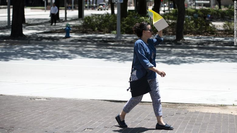 A pedestrian walks with a bag covering her face to block the sun during a heatwave in Houston, Texas. Photographer: Mark Felix/Bloomberg via Getty Images