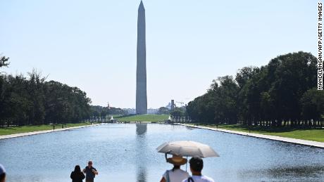 Le persone usano gli ombrelli per ripararsi dal sole mentre guardano il Monumento a Washington a Washington, DC sabato.