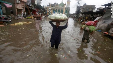Des travailleurs transportent des produits alors qu'ils traversent une route inondée après de fortes pluies, à Lahore, au Pakistan, le jeudi 21 juillet 2022. 